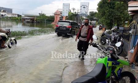 Kapolsek Glagah saat mengatur arus lalu lintas di jalan yang tergenang air dan masyarakat saat membersikan Enceng gondok.(IST)