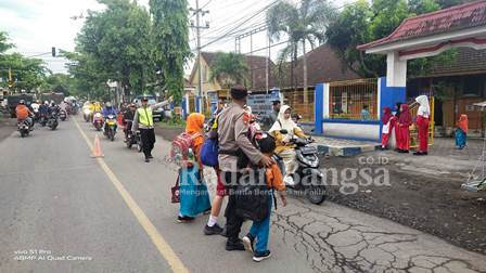 Anggota Polsek Pasirian saat Menyebrangkan siswa SDN Pasirian 1, Kamis (16/2). (Dok Humas Polres Lumajang, for Riyaman)