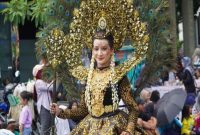 Seorang peserta karnaval tampil anggun dengan kostum bernuansa emas dan hiasan bulu merak dalam Mega Karnaval Kemerdekaan 2025 di Lamongan, Sabtu (23/8/2025). (Foto Dok Ho/RadarBangsa.co.id)