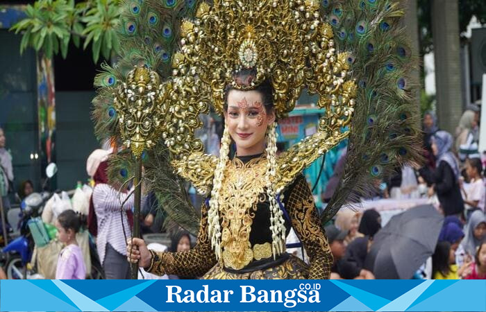 Seorang peserta karnaval tampil anggun dengan kostum bernuansa emas dan hiasan bulu merak dalam Mega Karnaval Kemerdekaan 2025 di Lamongan, Sabtu (23/8/2025). (Foto Dok Ho/RadarBangsa.co.id)