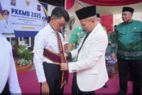 Wakil Bupati Pasuruan KH. Abdul Shobih (Gus Shobih) secara simbolis mengenakan atribut mahasiswa baru pada salah satu penerima beasiswa D3 Kebidanan dan Keperawatan dalam kegiatan PKKMB di Kampus Akademi Kebidanan Sakinah Pasuruan, Kamis (4/9/2025). (Dok foto Prokopim)